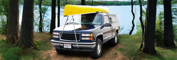 Truck in the outdoors on a dirt road with a canoe strapped to the top of the truck using master lock straps