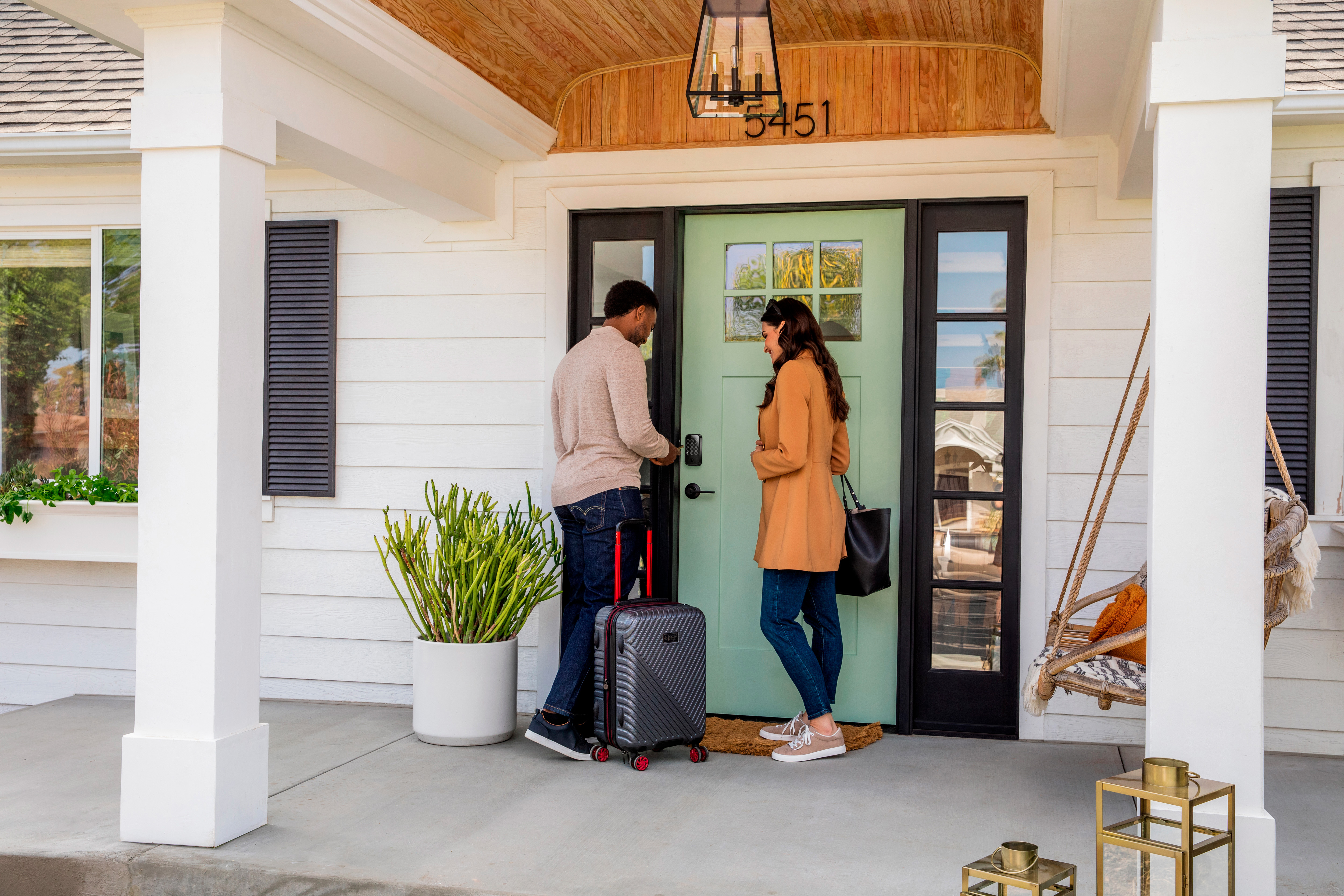 A man and woman lock their front door while they leave their house with luggage in tow